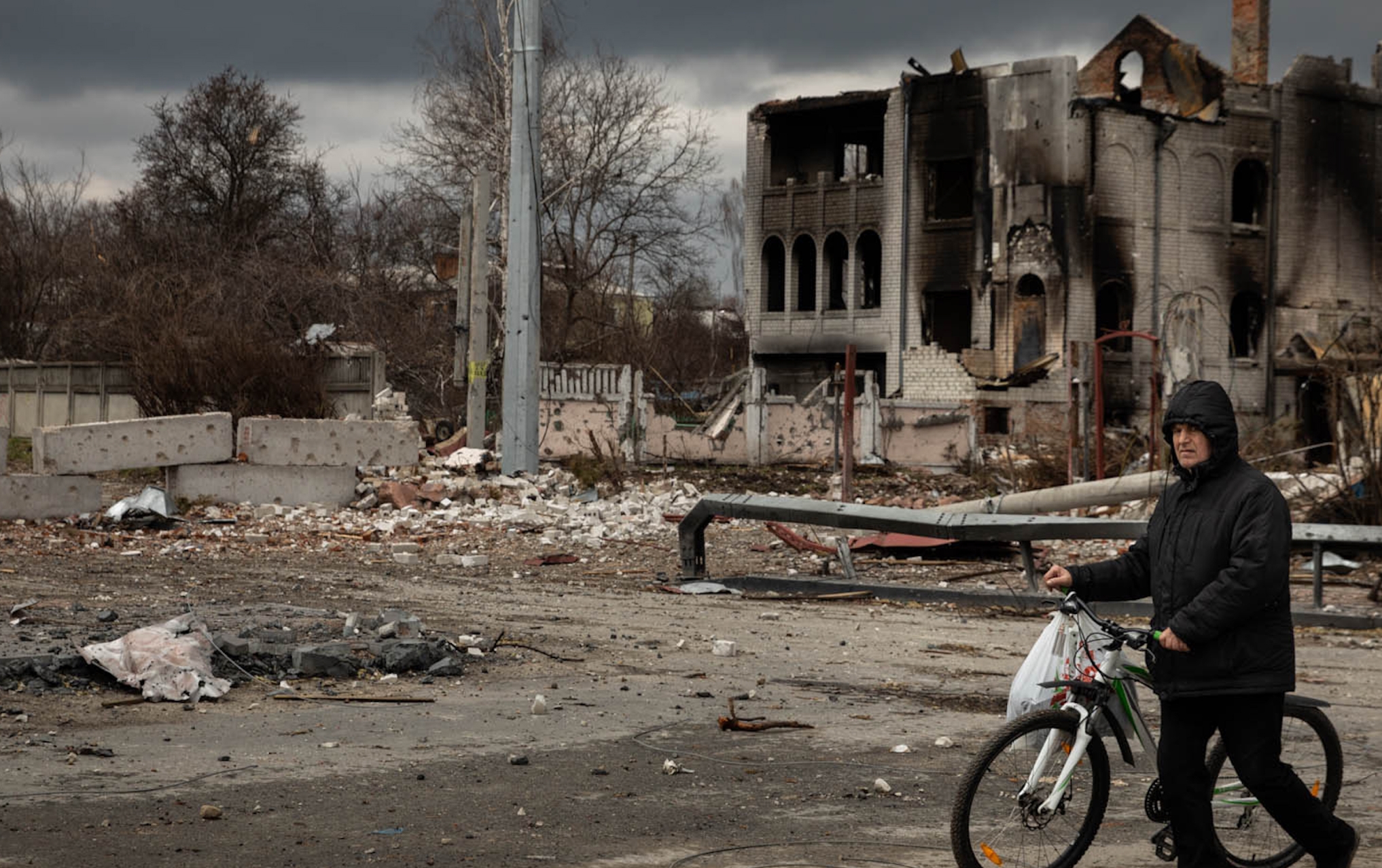 Man walks with a bike in front of a bombed building in Ukraine